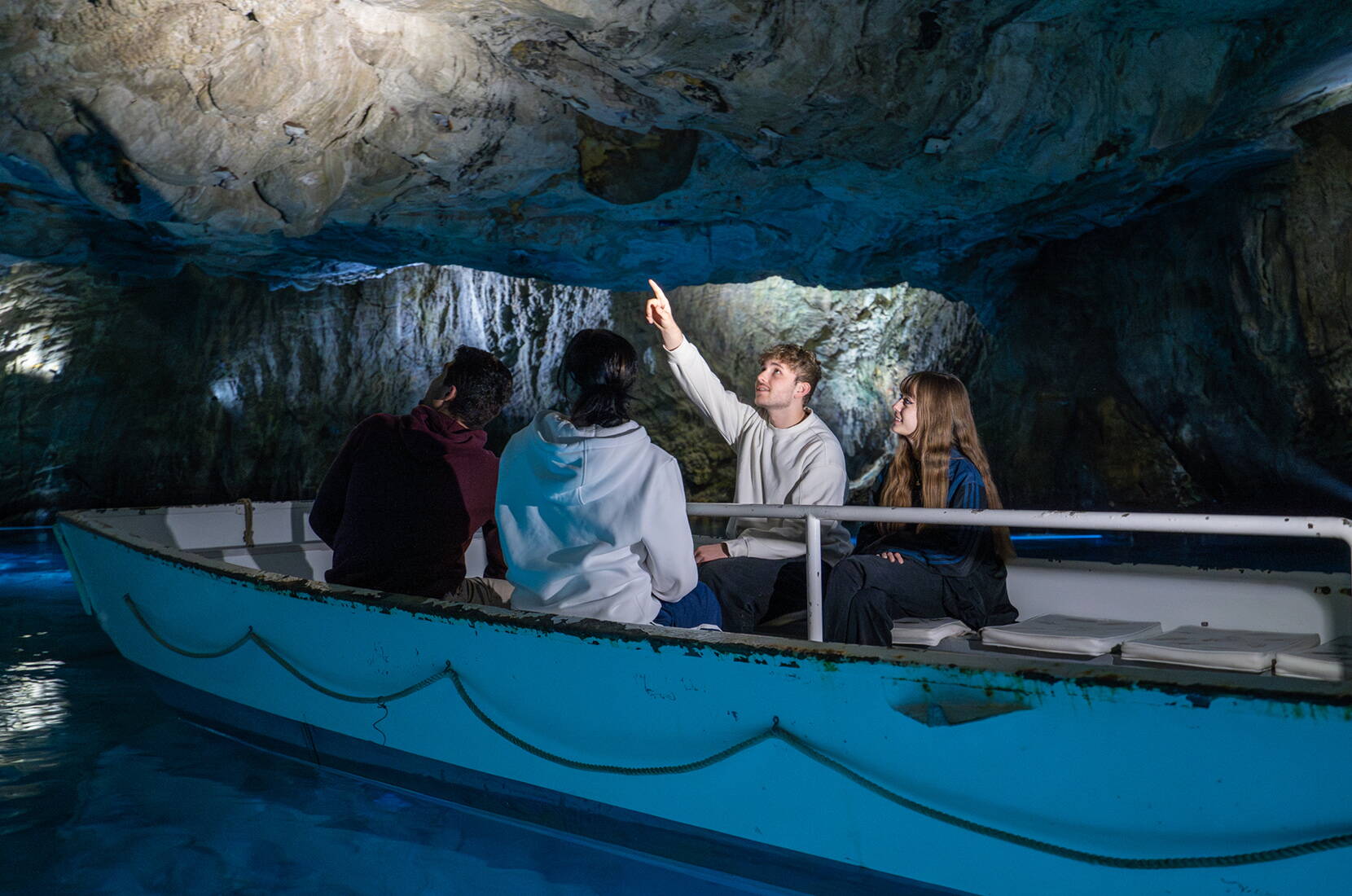 Eine Gruppe auf einem Boot entdeckt die Felsstrukturen des Lac Souterrain St‑Léonard während einer geführten Tour im unterirdischen See.