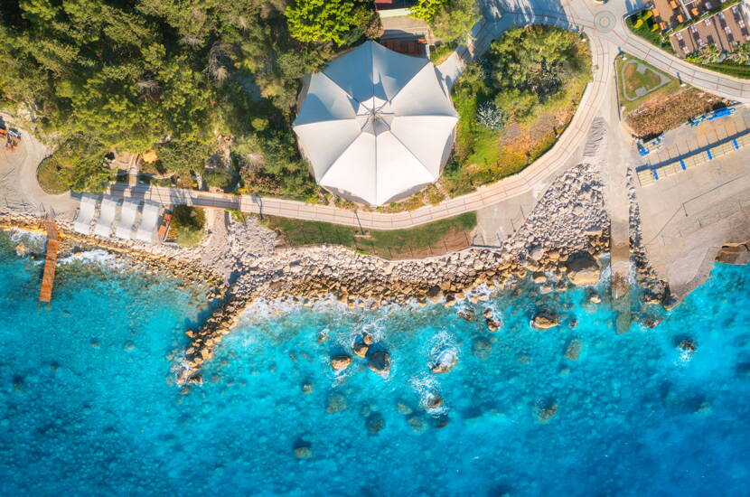 Zoom: Vogelperspektive auf eine Strandzone mit blauem Wasser und Felsformationen.