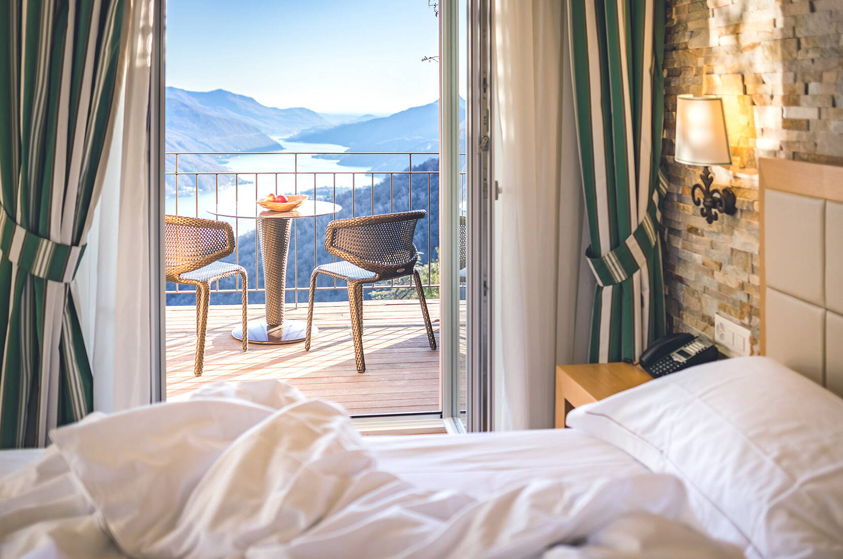 Chambre avec vue sur le lac et balcon Une chambre d’hôtel confortable avec accès direct au balcon, équipé de deux chaises et d’une table. La vue donne sur un lac et des montagnes environnantes sous un ciel dégagé.