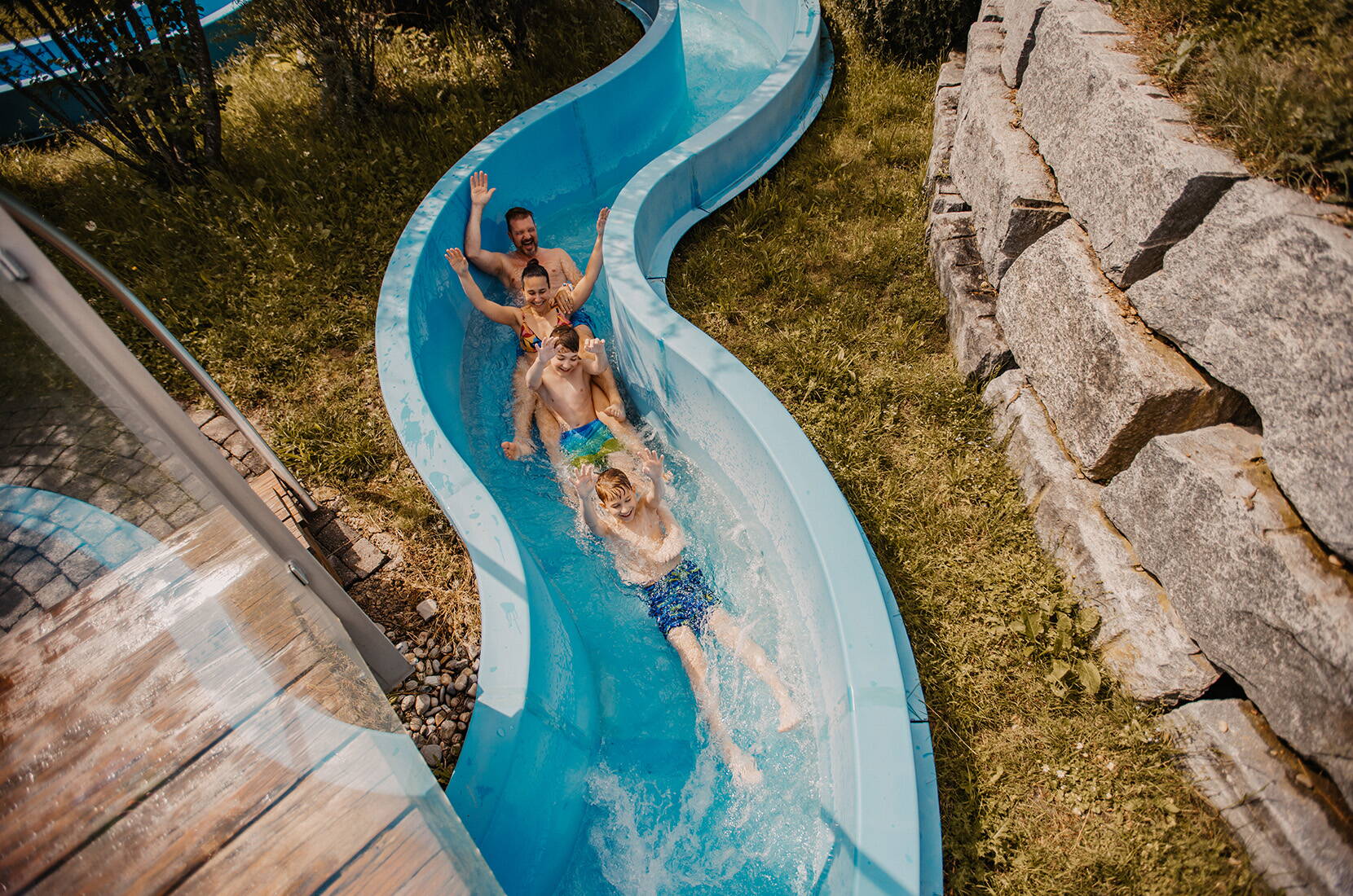 Un groupe de personnes descend ensemble le toboggan bleu extérieur.