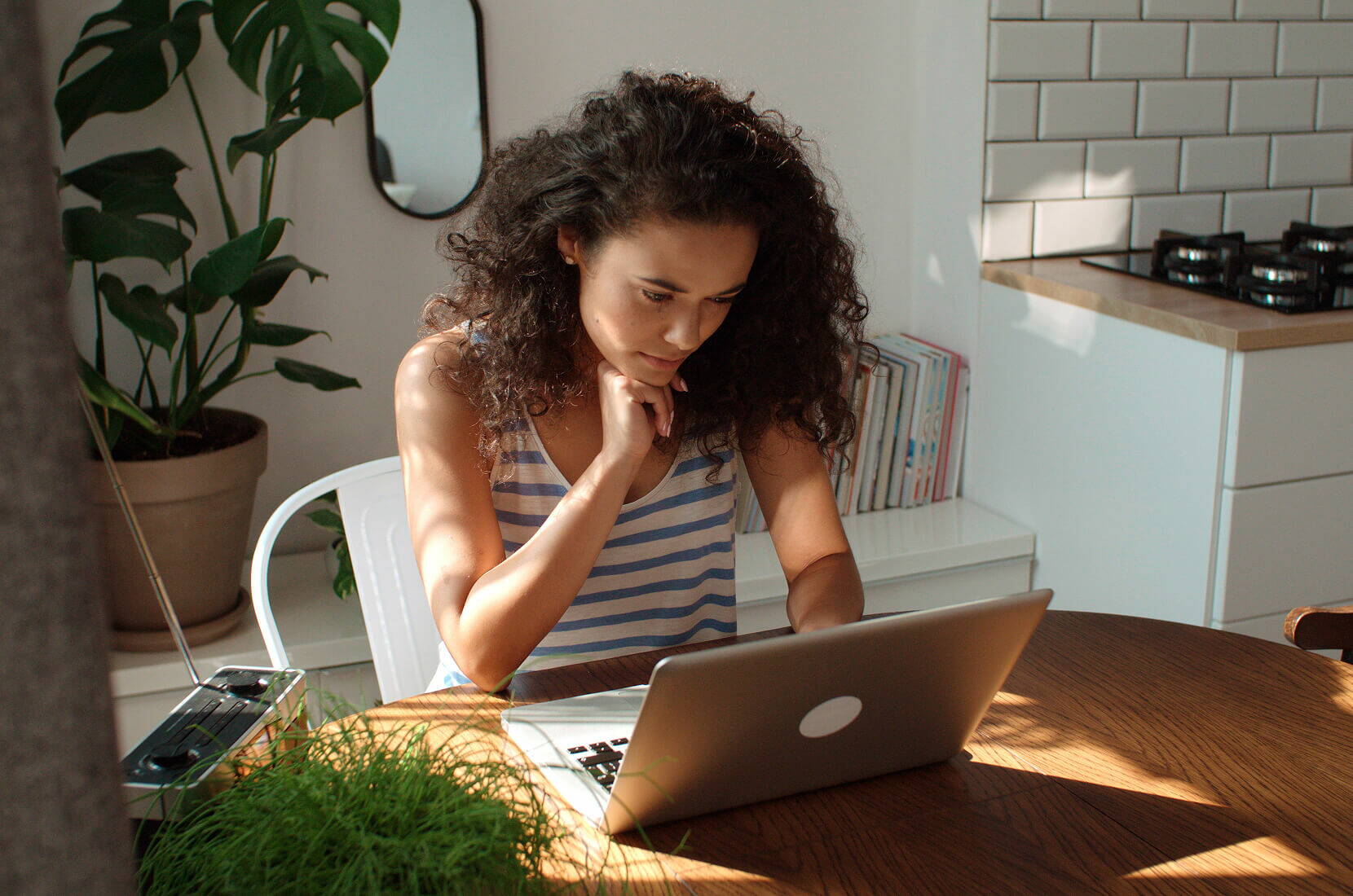 Persona che lavora al laptop in una stanza luminosa con piante sullo sfondo.
