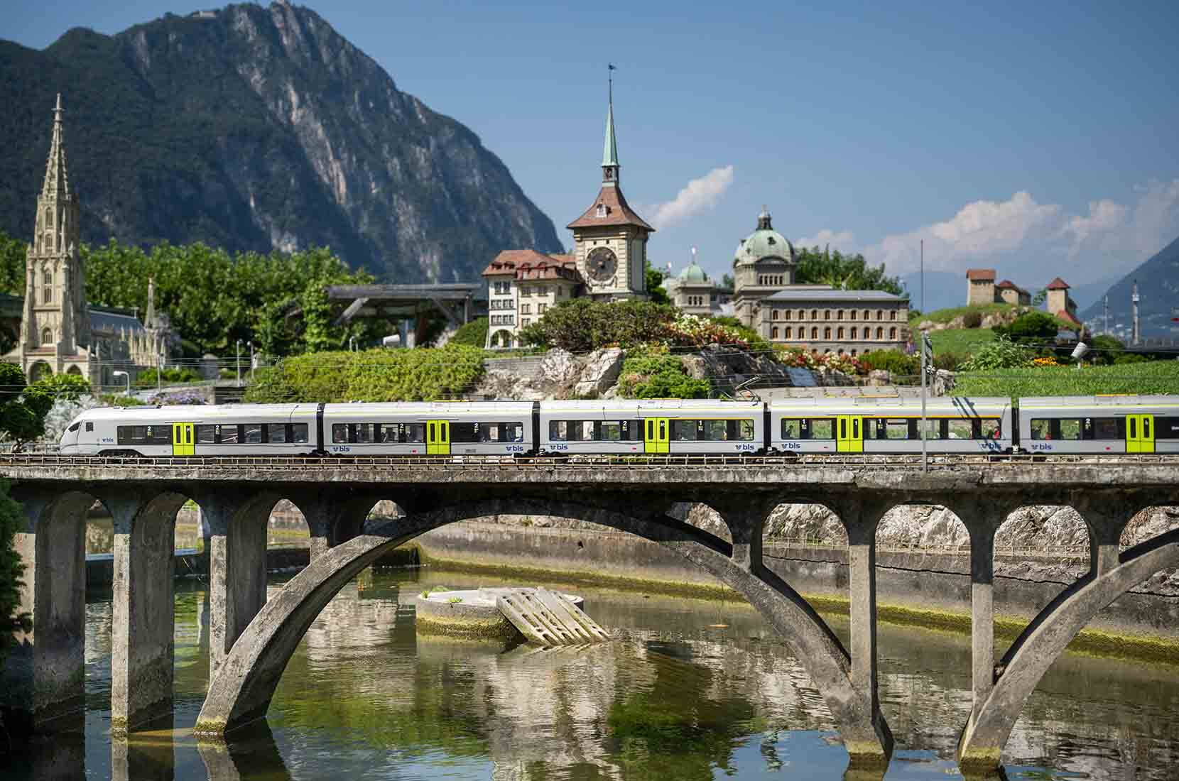 Un moderno treno regionale attraversa Swissminiatur. Sullo sfondo si distinguono la Cattedrale di Berna, la Torre dell’Orologio e il Palazzo federale riprodotti in miniatura.