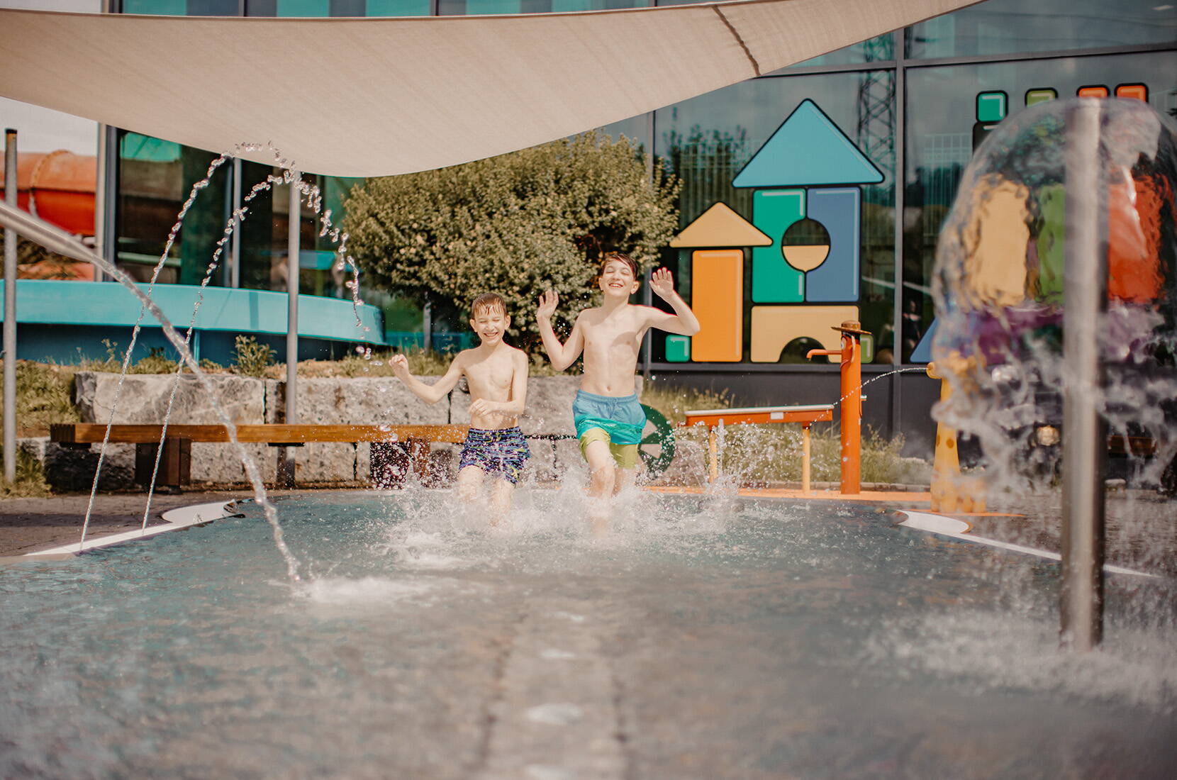 Kinder spielen im flachen Aussenbecken mit sprudelnden Fontänen.
