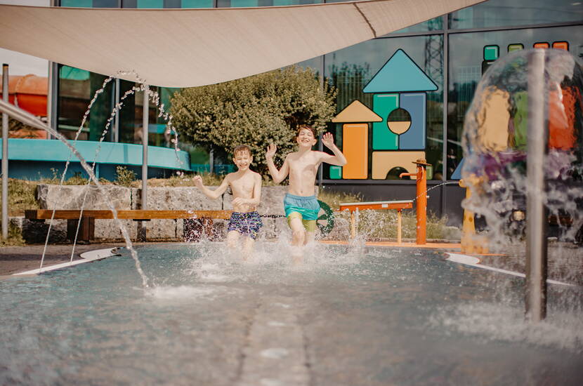 Zoom: Kinder spielen im flachen Aussenbecken mit sprudelnden Fontänen.