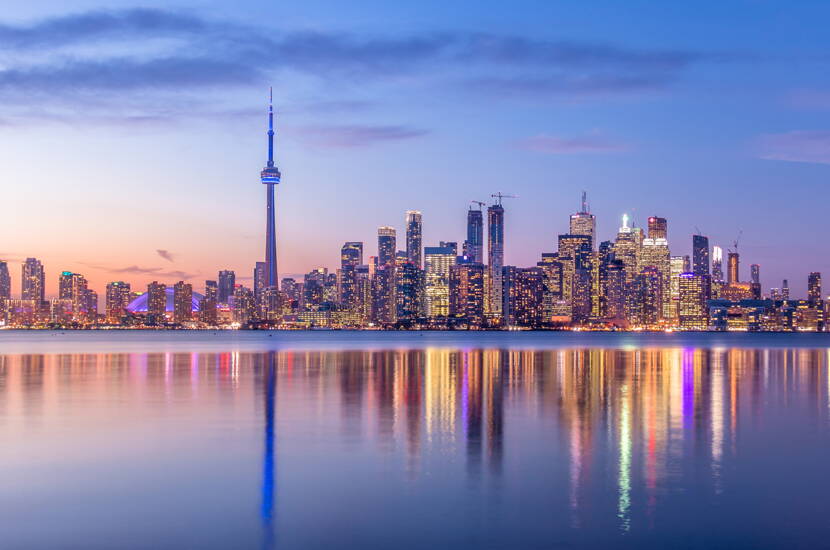 Zoom: Städtesilhouette mit reflektierenden Lichtern am Wasser bei Dämmerung.