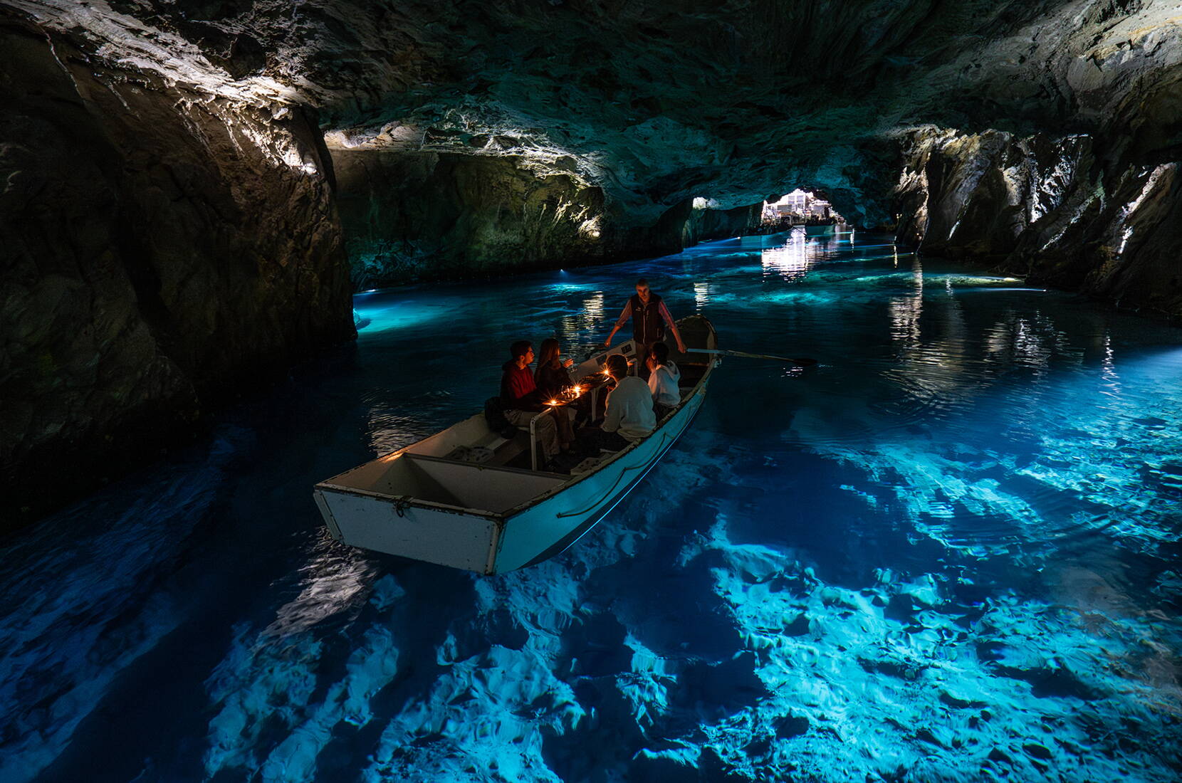 Una barca attraversa la grotta illuminata del Lac Souterrain St‑Léonard, mentre gli effetti di luce rendono l’acqua intensamente blu.