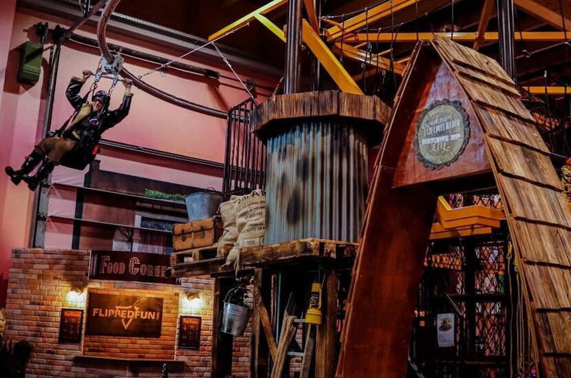 Zoom: Ein spannendes Zipline-Erlebnis führt quer durch die abenteuerlich gestaltete Indoor-Landschaft. Holzstrukturen, Requisiten und thematische Details sorgen für ein authentisches Erlebnis mitten im Funpark.