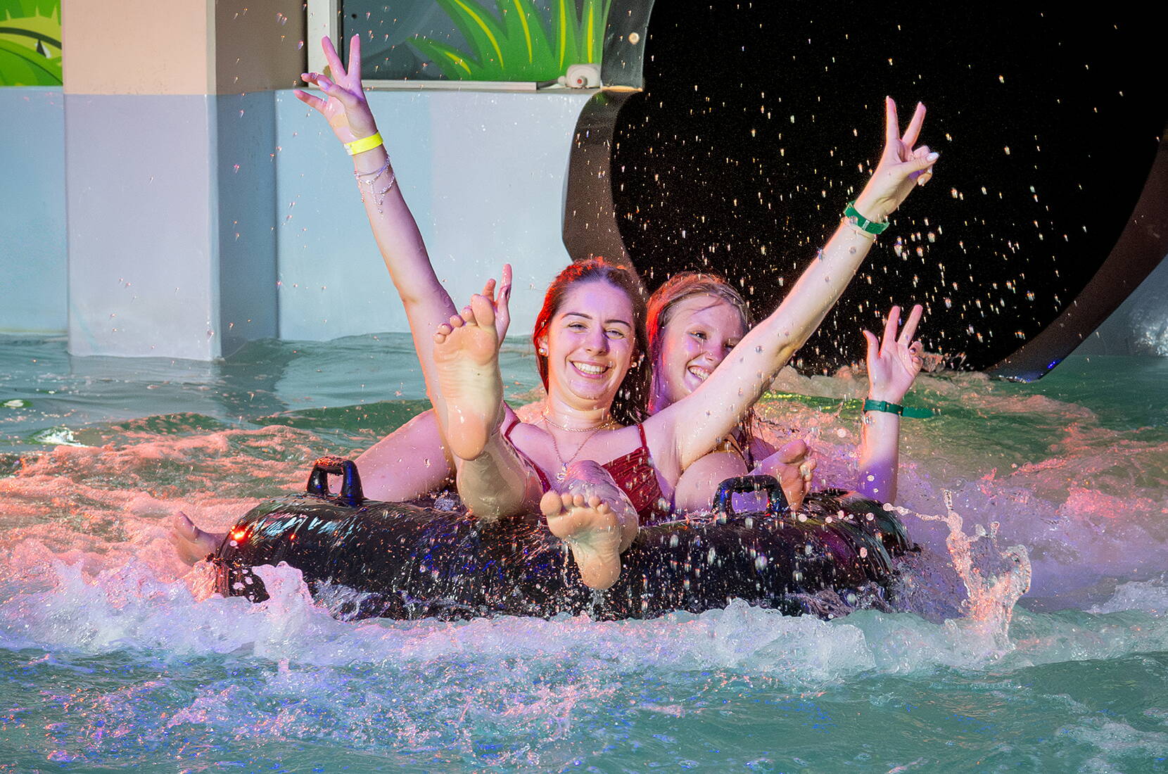 Zwei Personen tauchen mit erhobenen Armen und breitem Lächeln von einer Rutschbahn ins Wasser. Nervenkitzel garantiert im Aquaparc Le Bouveret!