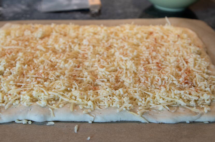 Pain farci au fromage Saupoudrer le fromage râpé sur la pâte posée sur le papier cuisson, puis recouvrir avec la deuxième moitié de pâte. Appuyer légèrement sur les bords.