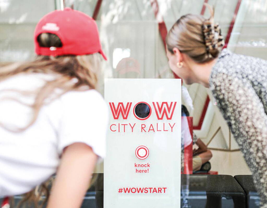 Zwei Personen vor einem Schild mit „WOW CITY RALLY“ und dem Knopf „knock here!“.