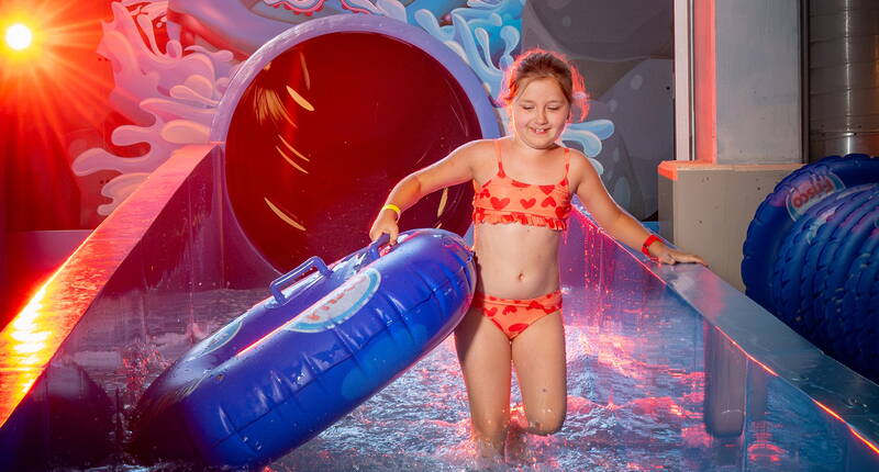 Un enfant sort d’un toboggan coloré avec une bouée bleue – l’aventure vous attend à l’Aquaparc Le Bouveret.