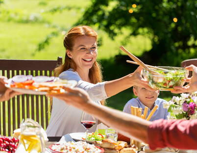 Familienessen im Garten Die Mutter reicht eine Schüssel mit frischen Salat an die Person gegenüber.