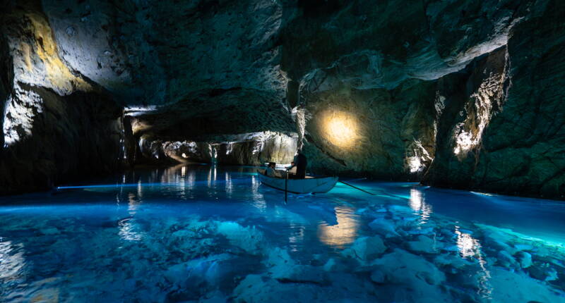 Una barca a remi attraversa l’ampia grotta del Lac Souterrain St‑Léonard, circondata da pareti rocciose e acqua blu.