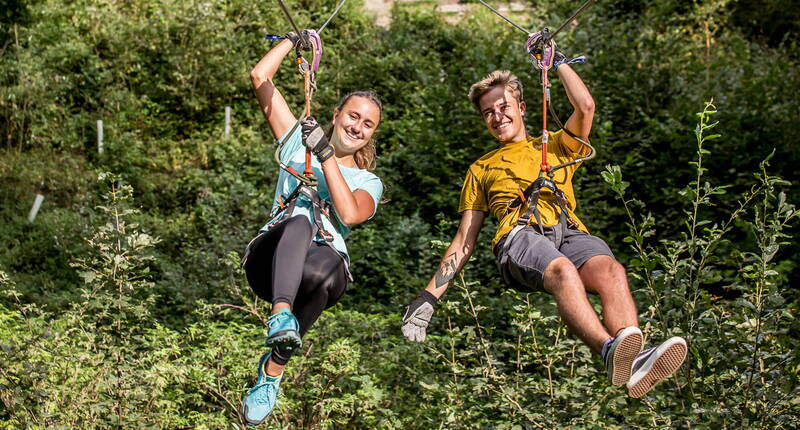 Zwei Personen gleiten nebeneinander auf einer Zipline durch den Seilpark Interlaken – ein actionreiches Outdoor‑Erlebnis für Abenteuerfans.