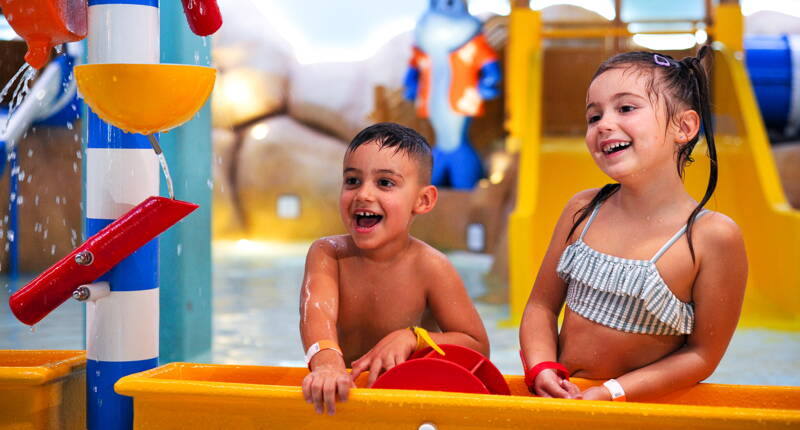 Zwei Kinder geniessen den farbenfrohen Wasserspielbereich mit Rutschen und spritzenden Elementen.