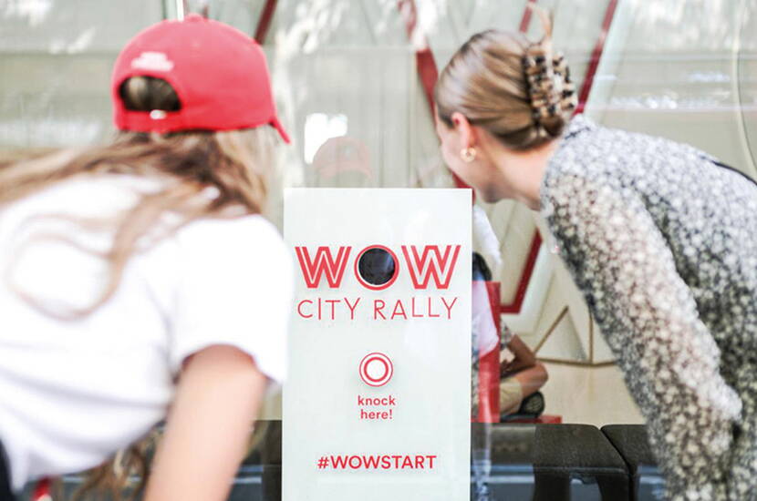 Zwei Personen vor einem Schild mit „WOW CITY RALLY“ und dem Knopf „knock here!“.
