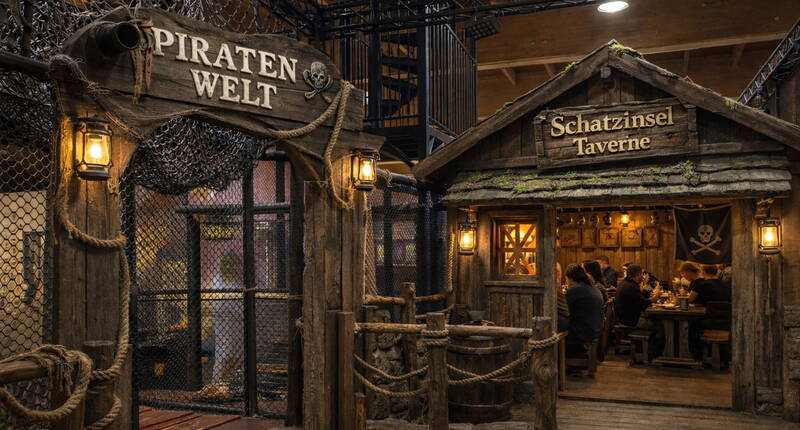 Le Monde des Pirates offre un décor rustique et immersif avec des filets, des lanternes et des éléments en bois. Dans la Taverne de l’Île au Trésor, les visiteurs profitent d’une ambiance chaleureuse comme sur une véritable île de pirates.