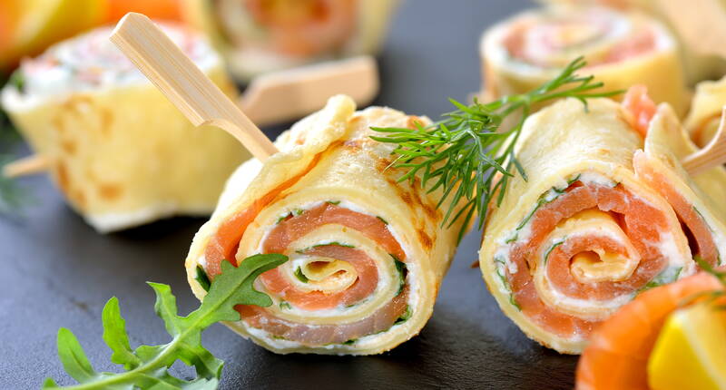 Prépare la pâte et fais cuire les crêpes dans du beurre. Nos crêpes roulées pour l'apéritif sont fourrées de saumon fumé, de fromage frais, de crème fraîche et de roquette. Elles peuvent être servies à l'apéritif ou comme plat principal avec une salade. La recette parfaite pour les jeunes et les moins jeunes. 