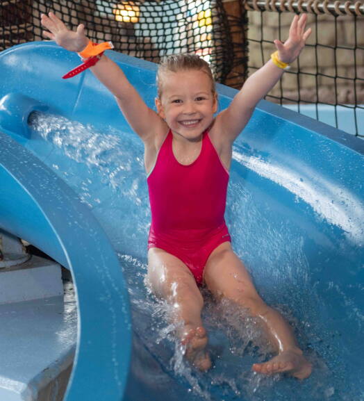 Un bambino scivola su uno scivolo d’acqua in una piscina avventura – idea perfetta per una gita in famiglia conveniente in Svizzera con promozioni o buoni gratuiti.