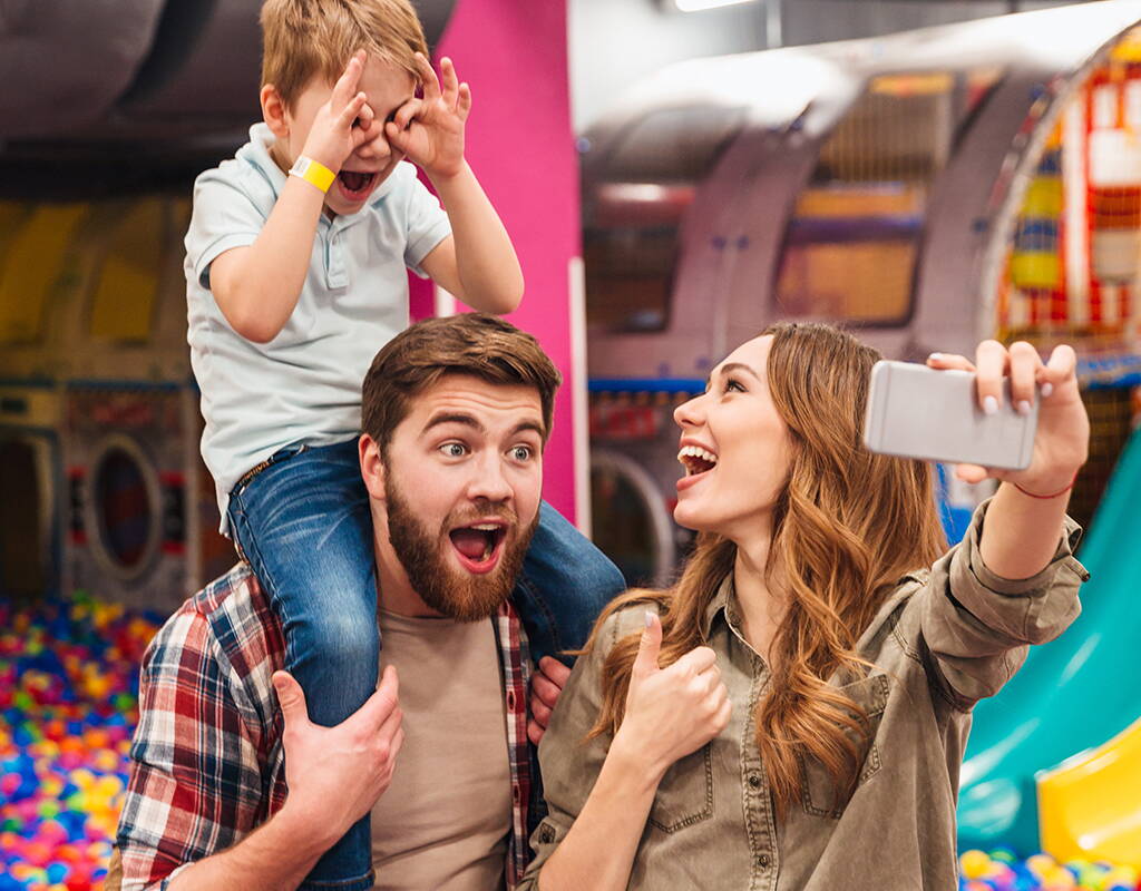 Familie im Indoor-Spielplatz Eltern mit Kind im Indoor-Spielplatz schiessen ein Selfie. Der Sohn sitzt auf den Schultern des Vaters.
