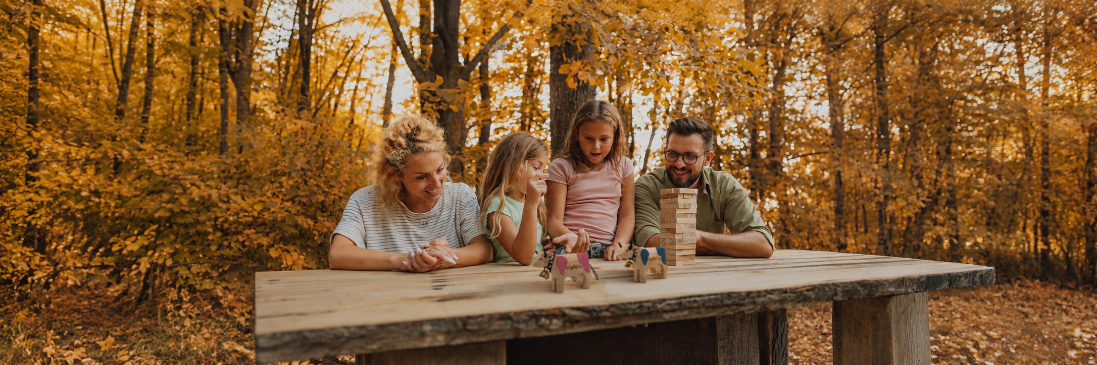 Familie spielt gemeinsam am Tisch in der Natur und entdeckt spielerisch die MiBon‑Kühe als Teil des Freizeitportals für entspannte Ausflüge in der Schweiz.