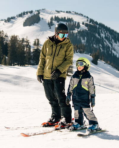 Zwei Personen geniessen das Skifahren in einer verschneiten Berglandschaft mit strahlendem Sonnenschein.