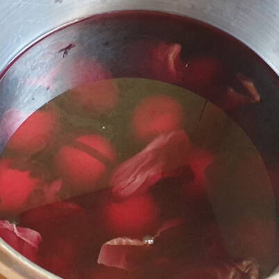 Une casserole contenant un bain colorant rouge‑bleuté à base de chou rouge, dans lequel plusieurs œufs sont immergés.