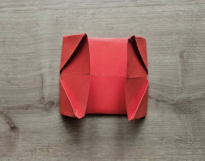 Papierportemonnaie falten – Seitenteile nach innen eingeklappt Die seitlichen Flügel des gefalteten Papiers werden nach innen eingeschlagen, wodurch sich die Grundform des Papierportemonnaies weiter verdichtet. Dieser Schritt definiert die spätere Innenstruktur des DIY Geldbeutels und sorgt dafür, dass die Fächer später stabil bleiben. Die diagonalen Faltkanten unterstützen die typische Origami‑Formgebung.