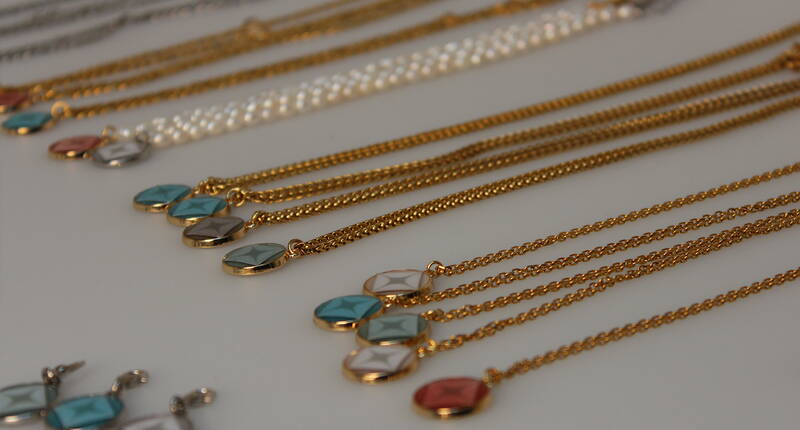 Plusieurs colliers et pendentifs LIORA dans différentes couleurs et variantes sont posés les uns à côté des autres. La collection montre à quel point tu peux composer ton bijou souvenir personnel de manière variée.