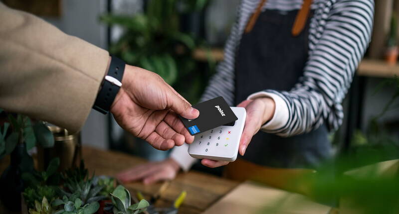 Une main tient une carte poinz devant un terminal de paiement pour un paiement sans contact.