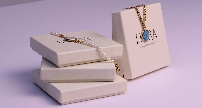 Un bracelet LIORA et un collier sont élégamment posés sur des boîtes à bijoux empilées. Les designs de haute qualité allient style, émotion et technologie NFC moderne.