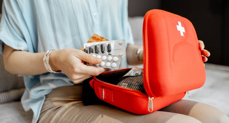 Eine Person sortiert Medikamente und verstaut sie in einer roten Erste-Hilfe-Tasche. Das Bild steht für eine gut organisierte Reiseapotheke.
