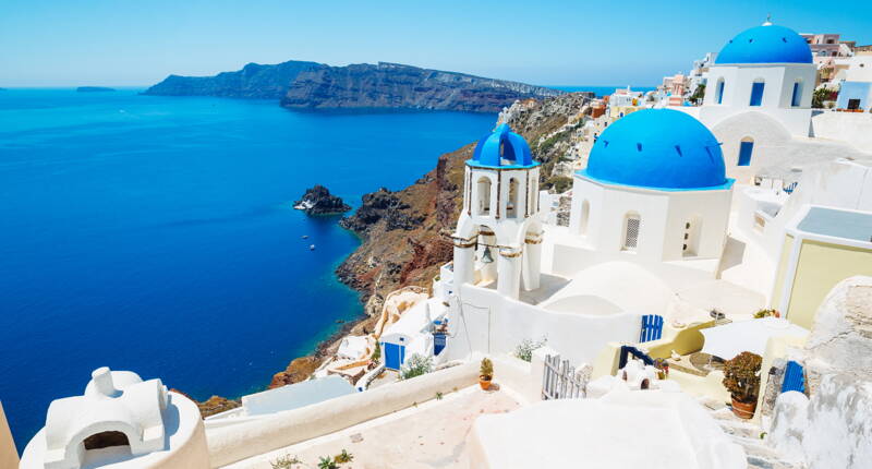 Küstenlandschaft mit typischen weiss‑blauen Gebäuden und Blick auf die Ägäis.