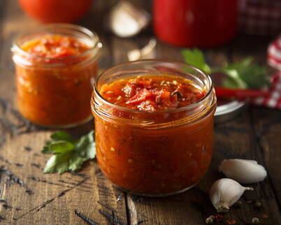 Zwei Gläser mit würzigem Tomatensugo stehen auf einem rustikalen Holztisch – ideal zum Einmachen und Lagern für die Winterküche.
