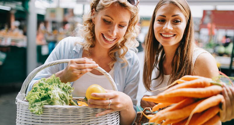 Zwei Personen kaufen auf einem Markt saisonales Gemüse ein – ein Symbol für bewussten Genuss und nachhaltige Ernährung.