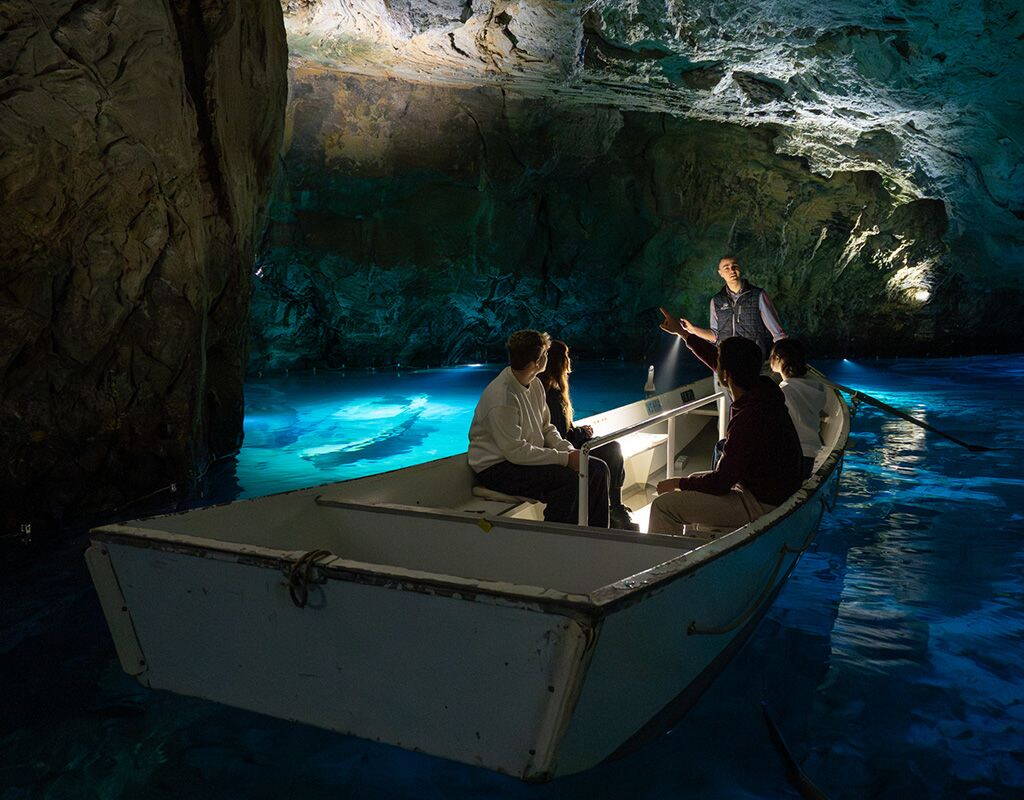 Trois personnes sont assises dans une barque à rames, guidée par un employé, glissant à travers la grotte éclairée du Lac Souterrain de St‑Léonard. Une expérience naturelle indoor unique dans le Valais.