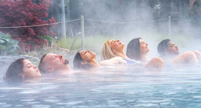 Gäste geniessen das wohltuende Thermalwasser im dampfenden Aussenbecken des Alpamare.