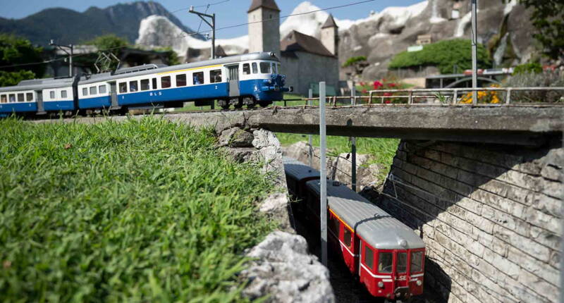 Un train BLS franchit un pont tandis qu’un train rouge des RhB circule sur la voie située en contrebas. Ces modèles reproduisent fidèlement le trafic ferroviaire suisse.