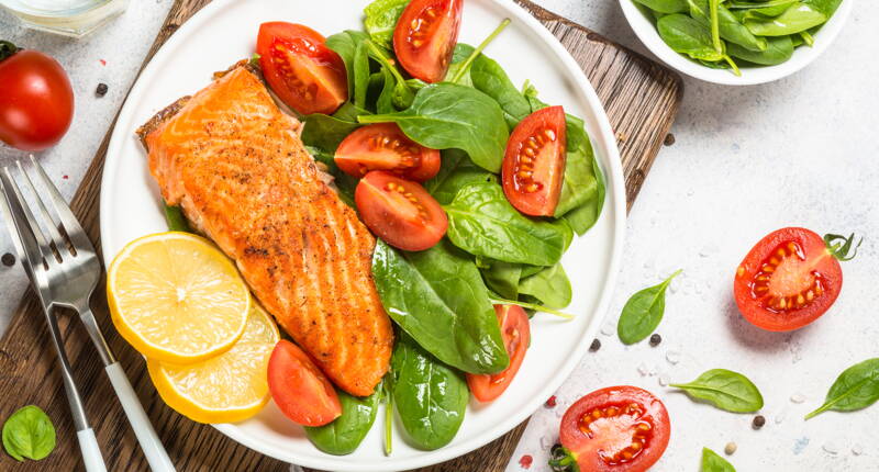 Salmone grigliato con spinaci freschi e pomodori su piatto bianco – cena sana ideale per dimagrire