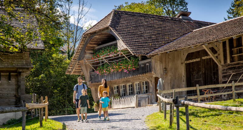 Une famille se promène sur un chemin naturel au Musée en plein air du Ballenberg. La maison traditionnelle et l’environnement paisible invitent à une visite conviviale et proche de la nature.