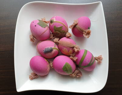 Des œufs fraîchement colorés en rose avec de fins motifs végétaux reposent sur une assiette et doivent encore être déballés.