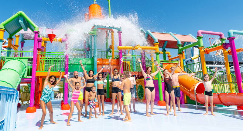 Des enfants et adultes s’amusent sous un seau géant d’eau dans l’univers coloré d’Aquaparc. Une expérience rafraîchissante et inoubliable pour tous!