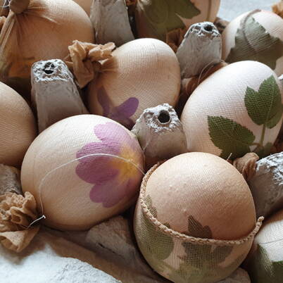 Mehrere Eier sind mit Blättern oder Blüten belegt und straff in Stoff oder Nylonstrümpfe eingewickelt, fixiert mit Faden.