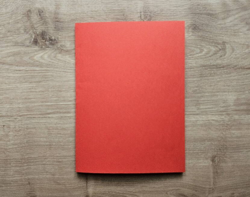 DIY Papierportemonnaie – Ausgangsmaterial rotes Papier Ein halbiertes rotes A4‑Papier liegt flach auf dem Tisch und bildet die Ausgangsbasis für das DIY Papierportemonnaie. Dieses rechteckige Papierstück ist der erste Schritt im Faltprozess und sorgt für eine saubere Grundlage für das spätere Origami‑Portemonnaie.