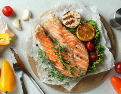 Bistecche di salmone su tagliere di legno con verdure Due bistecche di salmone su tagliere con verdure fresche e limone – ricche di Omega‑3 e ideali per la cena
