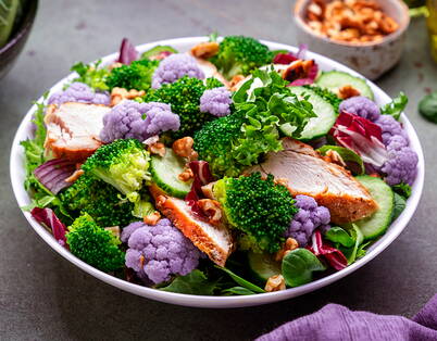 Farbiger Gemüseteller mit Poulet Auf dem Teller ist lila Blumenkohl, grüner Brokkoli und in Scheiben geschnittene Pouletbrust.
