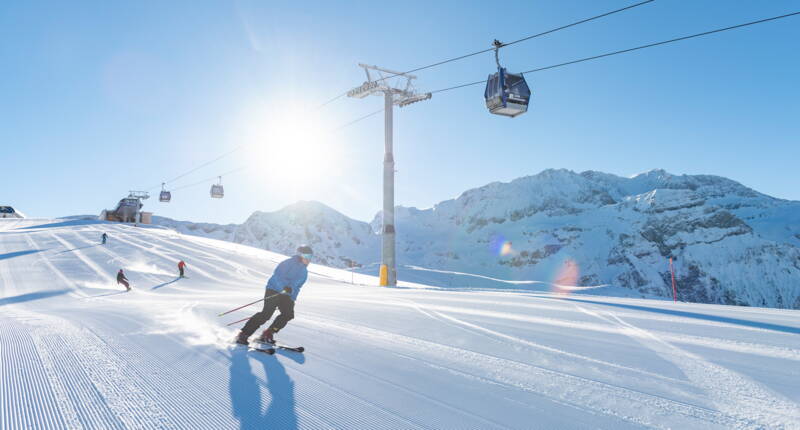 Ein Wintersportler fährt auf einer frisch präparierten Piste unter der Gondelbahn im Skigebiet Adelboden-Lenk. Das beliebte Skigebiet im Berner Oberland bietet abwechslungsreiche Abfahrten, moderne Bergbahnen und attraktive Skitageskarten.