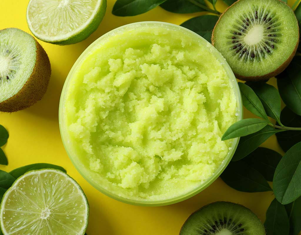 Ein leuchtend grünes Kiwisorbet in einer Schale, umgeben von aufgeschnittenen Kiwis, Limetten und grünen Blättern auf gelbem Hintergrund. Die frischen Früchte unterstreichen den sommerlichen und erfrischenden Charakter des Desserts.