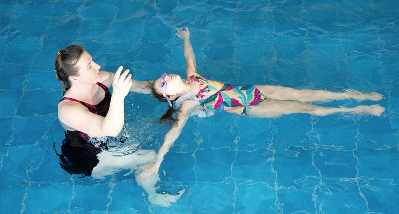 Un enfant pratique la position dorsale dans l’eau, accompagné par un adulte pour apprendre à flotter en toute sécurité.