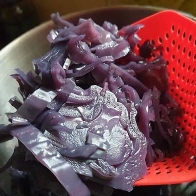 Strisce di cavolo rosso cotte e scolate riposano in un colino sopra una ciotola dopo la preparazione del decotto.